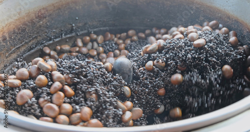 Canvastavla Chestnuts tumbling in hot black sand inside a rotating metal drum, traditional street food roasting process, Castanea sativa, commercial culinary production