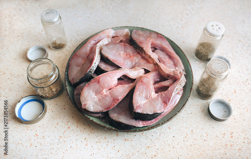 Large, freshly sliced pieces of silver carp are laid out on a green plate on the table. The concept is to prepare a fresh and healthy fish dish. Seasonings and dried herbs are also included.