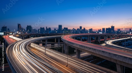 Highway interchange with light trails and modern city skyline at dusk