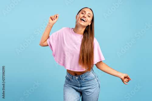 Happy young woman dancing  laughing on blue background