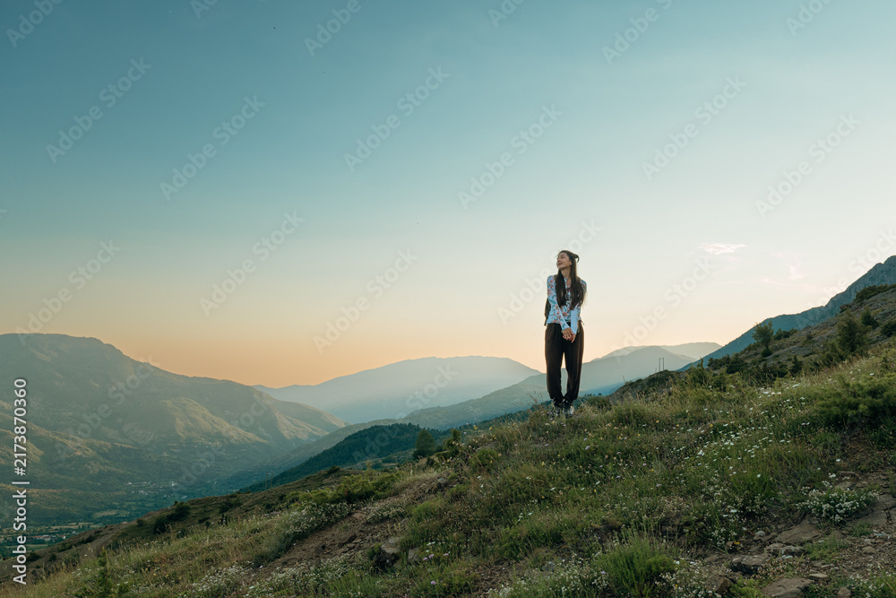 Obraz premium Young female hiker standing on a grassy mountain ridge enjoying the scenic valley view at sunset in Verri, Albania