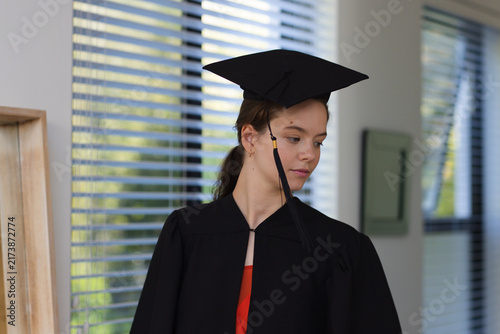 Canvastavla Adult female standing near window blinds wearing black grad gown and mortarboard