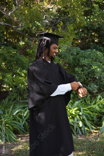Bild auf Leinwand Male graduate wearing black academic regalia and cap standing on campus lawn adj