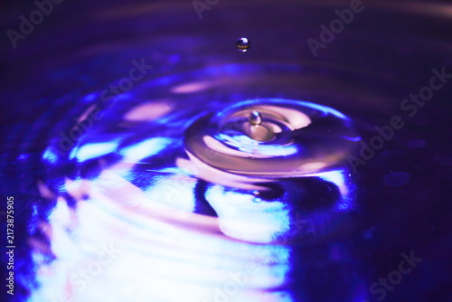 Water Drops Falling on Purple Blue Liquid Surface with Concentric Wave Ripples Close Up