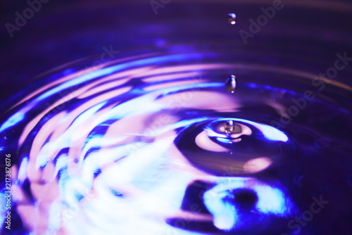 Water Drops Falling on Purple Blue Liquid Surface with Concentric Wave Ripples Close Up