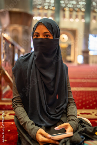 Фотография Muslim woman wearing niqab and hijab using phone in mosque