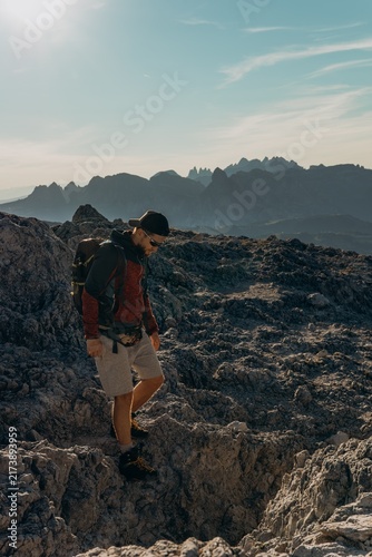 Foto Man with a backpack hikes down a rocky mountain ridge under a bright hazy sky
