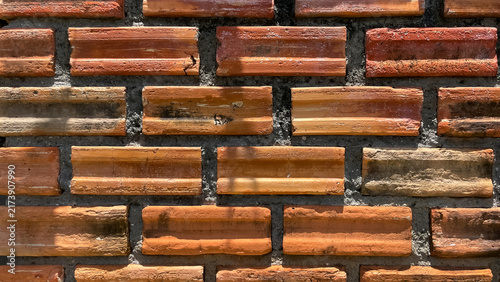A close-up of an old brick wall with rows of terracotta bricks and dark mortar joints. Detailed surface texture and natural signs of wear are visible.