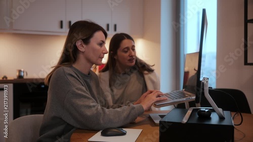 Woman working on laptop at home while another person organizes behind her