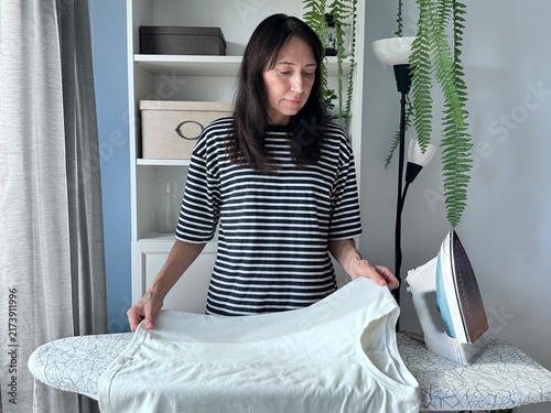 Canvastavla Female homeowner ironing a white bedsheet in a tidy living space with indoor plants