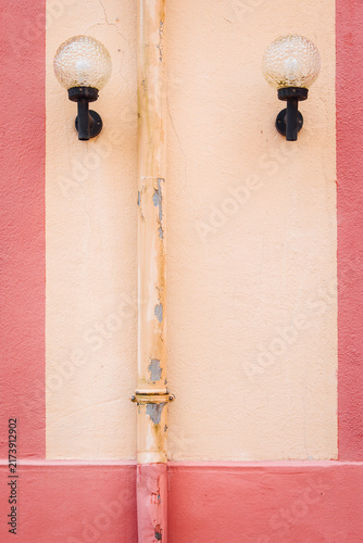 Luminaires sur un mur rose et crème avec un chéneau descendant. Mur graphique. Lampes extérieures sur une façade. Appliques vintage