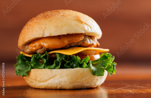 Delicious cheeseburger layer with golden bun juicy meat beef or pork patty melted cheddar cheese on wooden table background fresh ingredients green lettuce tomatoes tasty classic burger junk fast food