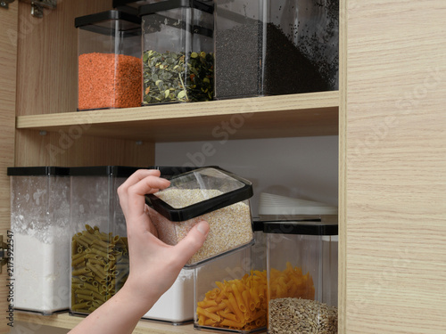 An open kitchen cabinet with shelves containing food, dry bulk products arranged in sealed plastic containers.
