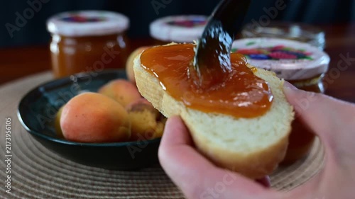 A person holds a piece of bread with apricot jam.