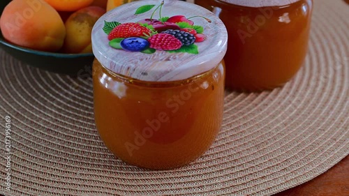 A glass jar of apricot jam sits next to a bowl filled with fresh whole and halved apricots.