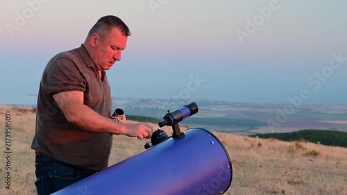 A man adjusts a telescope outdoors at sunset.