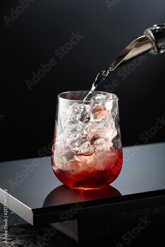 To make a Tequila Sunrise cocktail on a black table in bar.