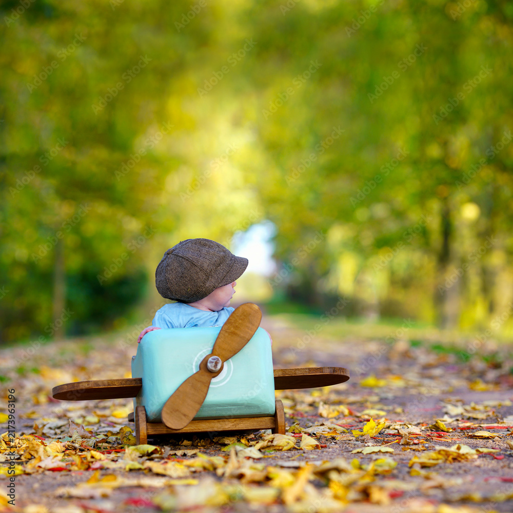 Naklejka premium Little Boy Playing Pilot in a Wooden Airplane on an Autumn Avenue