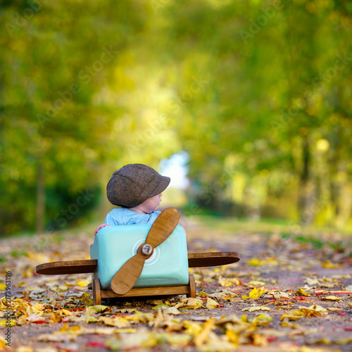 Little Boy Playing Pilot in a Wooden Airplane on an Autumn Avenue