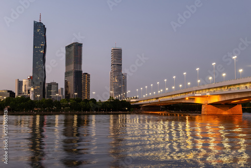 Modern city skyline with skyscrapers and illuminated bridge reflected in the river at twilight