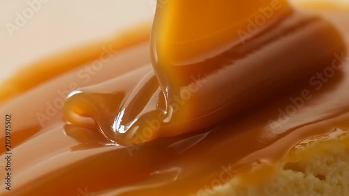 Slow motion close up of caramel sauce pouring and folding over pastry surface on plate in studio kitchen setting