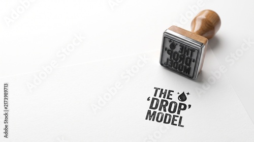 Vintage wooden rubber stamp with The Drop Model text. Professional business branding on white paper. Minimalist corporate identity mockup.