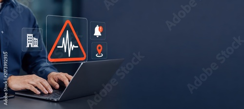 Seismic Alert System: A person uses a laptop to monitor seismic activity, with digital alerts and icons representing earthquake detection and building safety displayed on a holographic interface.