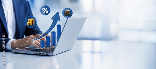 Digital Growth Chart: A businessman in a sharp blue suit works on a laptop, symbolizing financial success and business growth with an upward-trending bar chart and percentage icon.