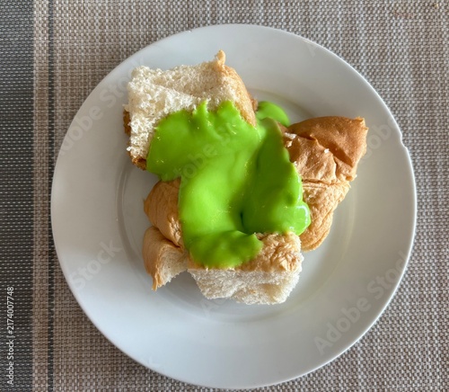 Traditional Thai dessert of soft bread drizzled with sweet green pandan custard, served on a white plate as a popular local sweet snack.