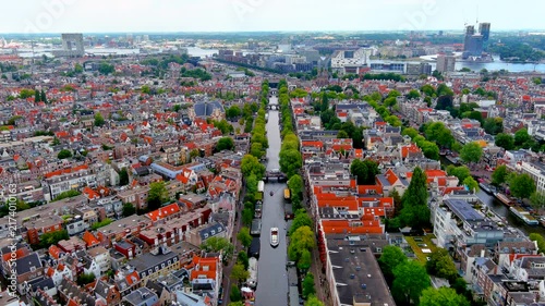 Aerial drone view of the Prinsengracht canal in Amsterdam with tour boats, the Noorderkerk church, Jordaan rooftops and the IJ harbor waterfront, Netherlands, in summer.