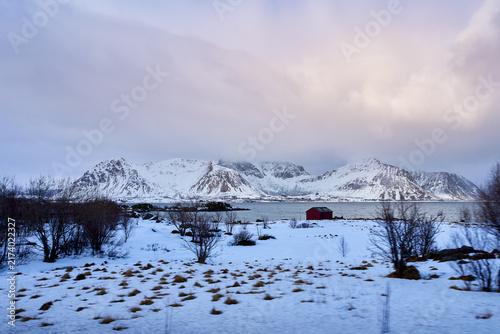 Beautiful scenic viewpoint of an iconic concrete bridge crossing the blue sea fjord in Lofoten, Norway. Majestic winter landscape with grand snow-covered mountains under a dramatic sky in Arctic Scand