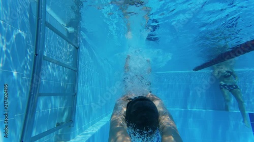 Slow motion underwater view of teenager diving headfirst into swimming pool