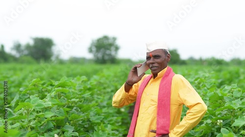 senior indian farmer talking on mobile phone at cotton agriculture field