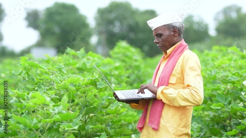Senior indian farmer using laptop at agriculture field