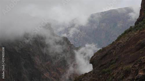 Dramatic moody fog swirling through rugged volcanic mountain peaks and deep steep valleys in Madeira island, creating an epic mystical wilderness landscape. 4K video.