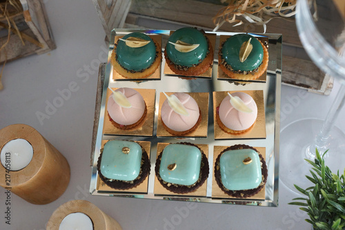 Set of festive miniature desserts with a glossy glaze in teal aqua and pink tones placed on a stand.Closeup top view.