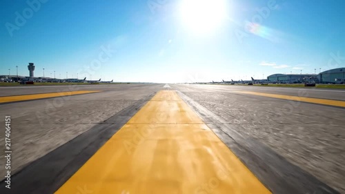Wide runway perspective with bright yellow centerline under clear sky at an airport.