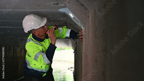 Worker Using Flashlight to Inspect Water Flow Inside Concrete Drainage Tunnel