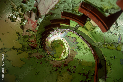 Abandoned overgrown mansion with spiral staircase, old car and ruined interior