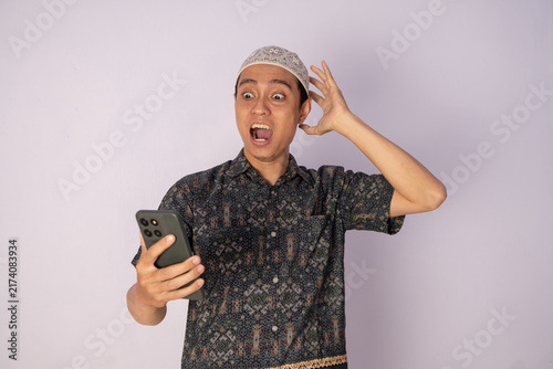 Surprised Young Man in Traditional Attire Holding a Smartphone in Shocked Expression