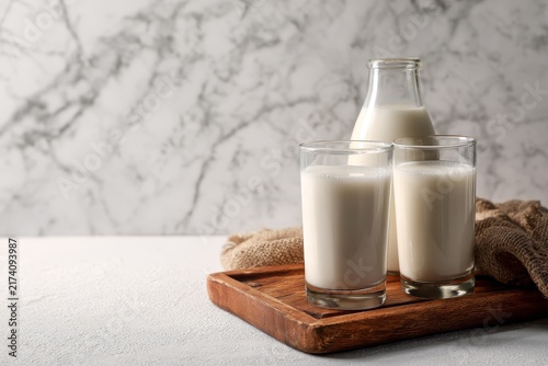 Fresh milk in glass bottles and drinking glasses on wooden tray, healthy dairy drink and natural breakfast nutrition concept.