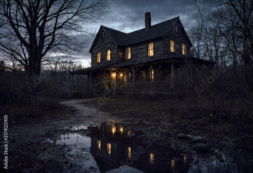 Dark eerie old wooden house at dusk with warm lights shining in a secluded forest area