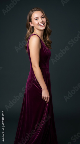 Woman in purple velvet dress smiling while looking at camera. Portrait, fashion, event, celebration, formal wear.
