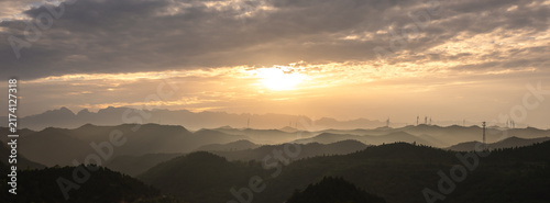 Sunrise Over Layered Mountains With Wind Turbines