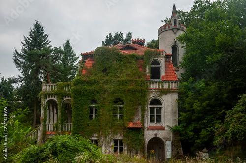 Abandoned overgrown mansion with spiral staircase, old car and ruined interior