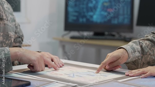 Military officers analyzing tactical map documents and digital tablet in command war room