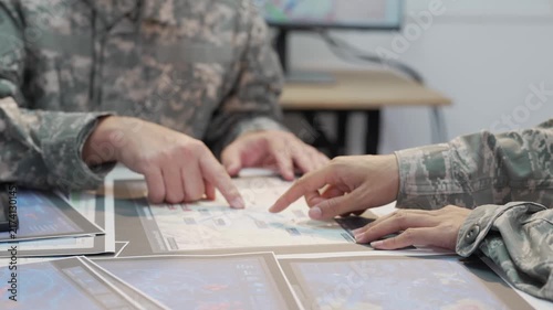 Military officers analyzing tactical map documents and digital tablet in command war room