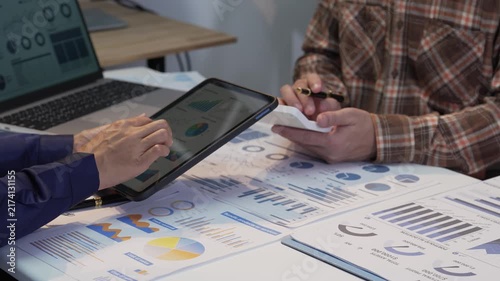 Business colleagues working together analyzing financial graphs on digital tablet and using calculator in office