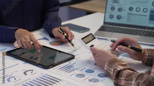 Business colleagues working together analyzing financial graphs on digital tablet and using calculator in office
