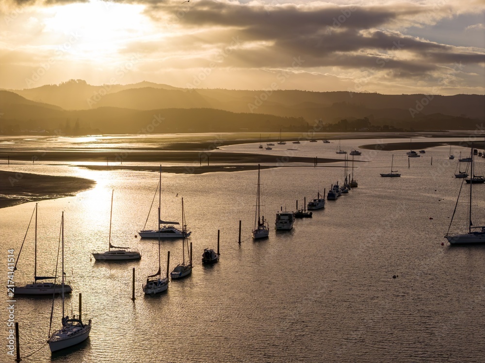Obraz premium Sailboats moored in the calm estuary waters at sunrise in Whangamata, Waikato, New Zealand, creating a peaceful coastal landscape view.